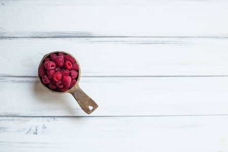 Bowl with summer raspberries on white wooden table. Empty space