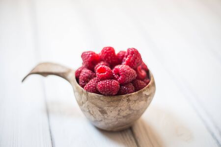 Wooden bowl with summer raspberries on white tableの写真素材