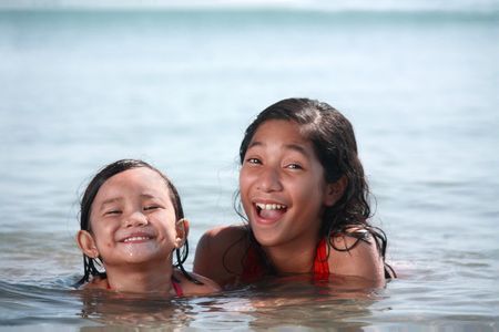 young asian kids enjoying a swim in the beachの写真素材