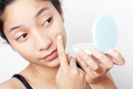 Teenager checking her face for pimple in the mirror.の写真素材