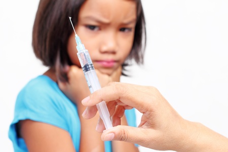 Close up view of a syringe with a child at the backround expressing fear of injection.の写真素材