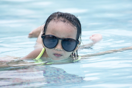 Portrait of a little girl with sunglasses enjoying the sun in the swimming pool.の写真素材
