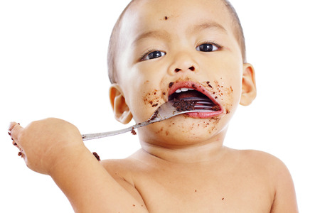 Portrait of a young boy eating cake crumbs with fork. Close up. Isolated in white background.の写真素材