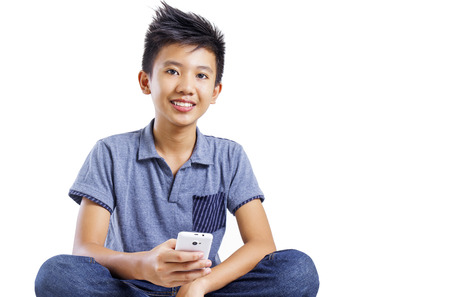 Relaxing asian boy holding a cellphone. Isolated in white background.の写真素材