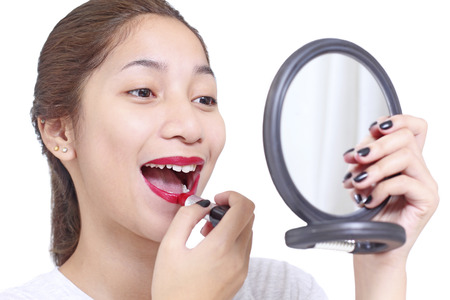 Asian lady looking into a mirror while applying lipstick. Isolated in white background.の写真素材