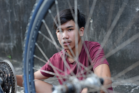 Asian boy looking through spokes of a bicycle tire.