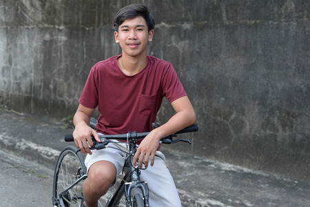 Young asian male teenager on a bicycle looking and smiling at the camera.の写真素材