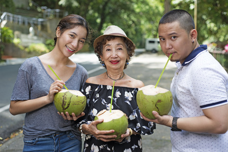 Senior woman with grandchildren enjoying fresh coconut juice. Outdoor summer picture by the...