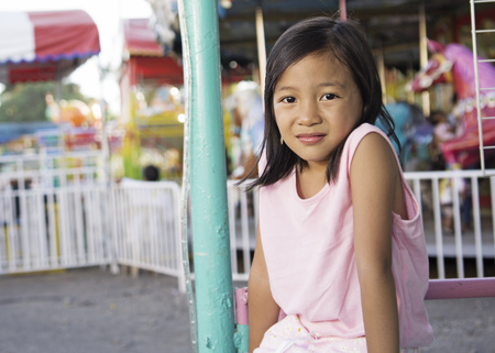 Portrait of a young girl sitting in the amusement park. Carousel at the background.の写真素材