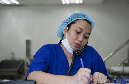 Asian nurse busy calling on the phone and taking notes of the conversation.の写真素材