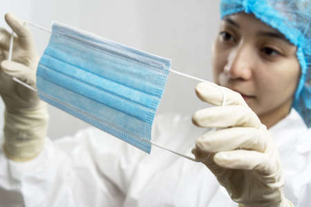 Asian nurse or doctor on personal protection equipment PPE inspecting a facemask.の写真素材