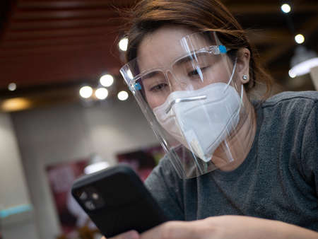 woman with facemask and face shield using a cellphone.の写真素材
