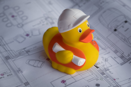 Rubber toy duck construction worker sitting on building plan. Easy building and construction concept. Safety, protection and planningの写真素材