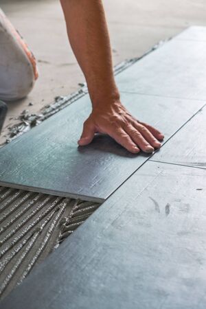 Worker placing ceramic floor tiles on adhesive surfaceの写真素材