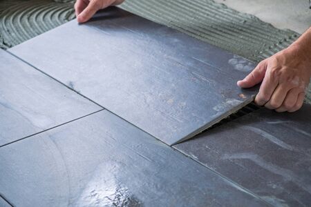 Worker placing ceramic floor tiles on adhesive surfaceの写真素材