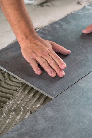 Worker placing ceramic floor tiles on adhesive surfaceの写真素材