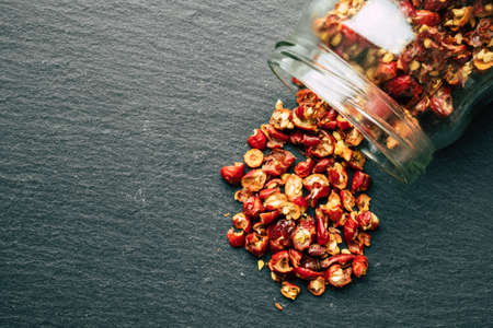 Wild rose hip dry fruit spilled on the black rock surface from glass jar
