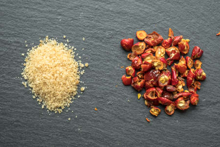 Wild rose hip dry fruit and pile of brown sugar on the black rock surfaceの写真素材