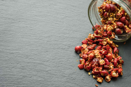 Wild rose hip dry fruit spilled on the black rock surface from glass jar