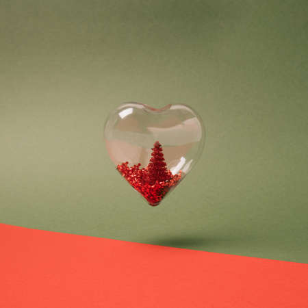 Heart shaped soap bubble with red Christmas tree inside floating over red and green bacground. Christmas love minimal conceptの写真素材