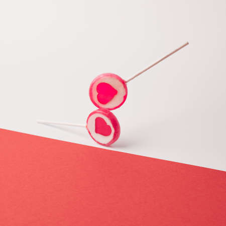 Two romantic pink lolipops touching on the red and white background. Valentines minimal studio shotの写真素材