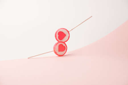 Two heart themed lolipops touching in the air over the two tone pastel pink background. Romance...