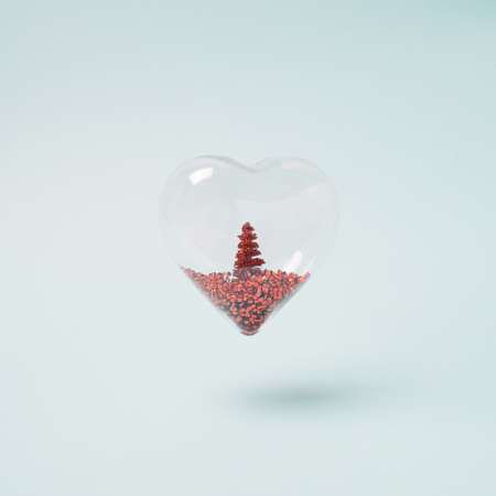 Heart shaped ornament with red glitter Christmas tree inside on the pastel blue background. Holiday love minimal concept.の写真素材