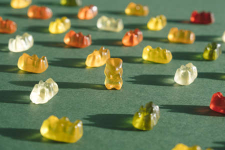 Yellow soft candy bear sitting on the dark green background. Unique minimal conceptの写真素材