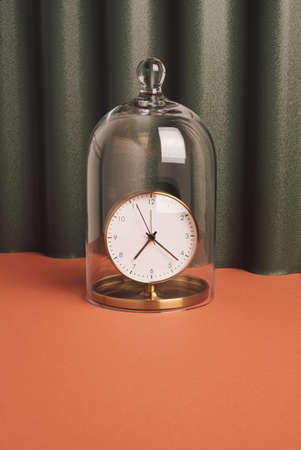 Vintage brass clock under the glass bell against pastel green and orange background. Precious time conceptの写真素材