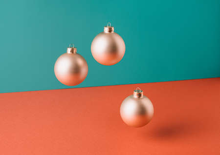 Floating golden Christmas tree baubles against two tone pastel background. Minimal New Year conceptの写真素材
