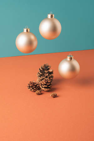 Floating Christmas tree gold baubles with tree cones underneath against two tone pastel background. New year minimal conceptの写真素材