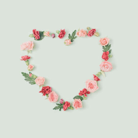 Spring flowers arranged in a shape of a heart on a pastel green background. Love and romance concept