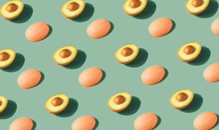Pastel orange painted avocado halves arranged on a pastel green background. Vegan diet minimal flat...
