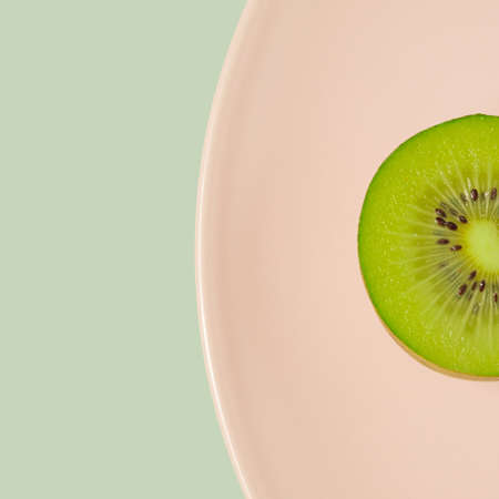 Kiwi fruit half macro shot on a pastel pink plate. Fruit diet minimal concept.の写真素材