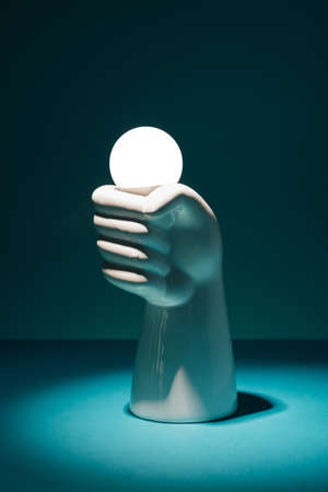 Concrete hand holding a light bulb on a dark background. Electricity, power minimal concept.の写真素材