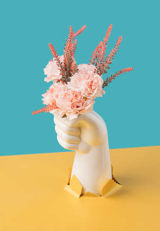 Artificial hand holding colorful flowers bursting through torn paper. Still life conceptual background.の写真素材