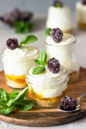 Homemade no baked dessert (cheesecake, trifle, mousse) with orange or peach jam in small portioned jars served with frozen berries and mint.