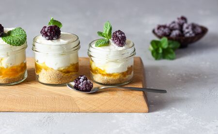 Homemade no baked dessert (cheesecake, trifle, mousse) with orange or peach jam in small portioned jars served with frozen berries and mint.の写真素材