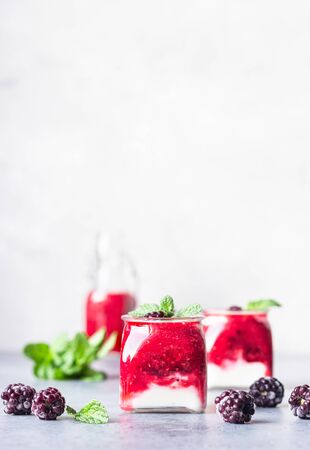 Glass jars of healthy layered berries and yogurt smoothie. Mix berry smoothie with raspberry, blackberry and yogurt. Wellbeing and weight loss concept. Selective focus, toned image.の写真素材