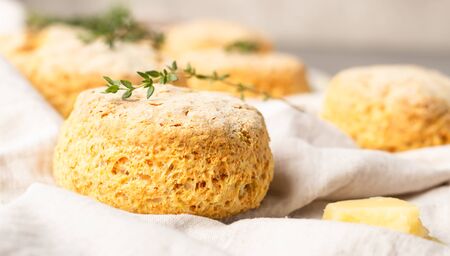 Cheese scones, pieces of cheese and thyme on a gray napkin. Gray stone background, toned image.