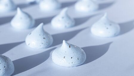 Mini blue meringue on blue paper background in sunlight dropping shadows. Creative concept. A...