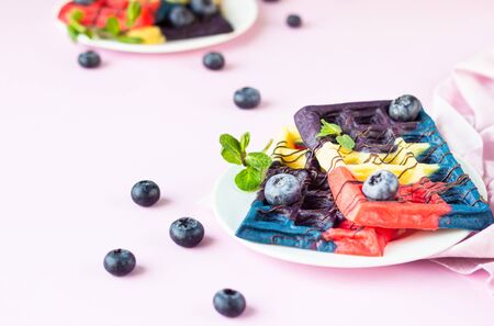 Colorful Belgian waffles decorated with chocolate glaze, fresh blueberries and mint. Pink paper background.の写真素材