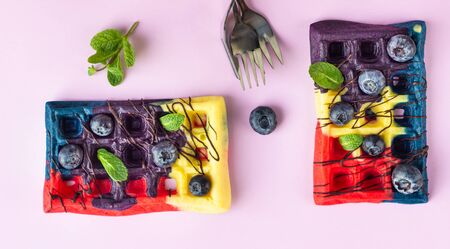 Colorful Belgian waffles decorated with chocolate glaze, fresh blueberries and mint. Pink paper background.の写真素材
