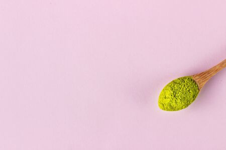 Wooden spoon with powdered matcha green tea on pink paper background. Superfood, healthy food concept.の写真素材