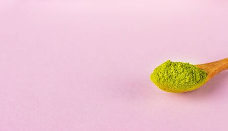 Wooden spoon with powdered matcha green tea on pink paper background. Superfood, healthy food...