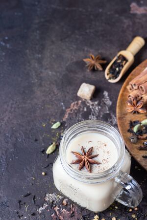 Mason jar with traditional Indian masala chai tea on dark stone background. Spiced hot tea with milk and spices for making tea - cinnamon, anise, cardamom, nutmeg, pepper and brown sugar.の写真素材