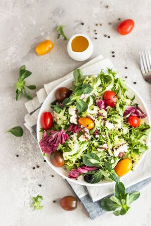 Green mix salad leaves with colored cherry tomatoes, ricotta or feta cheese and balsamic in a white ceramic plate on a light gray background. Healthy food concept.の写真素材