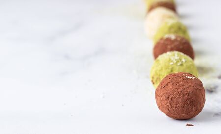 Raw energy balls with matcha tea powder, cocoa powder and coconut flakes, light gray background....
