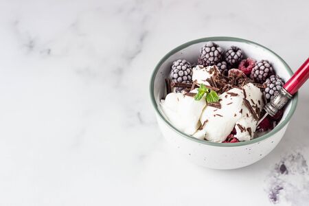 Vanilla ice cream with frozen raspberries, blackberries, chocolate and mint in a ceramic bowl, light gray background.の写真素材
