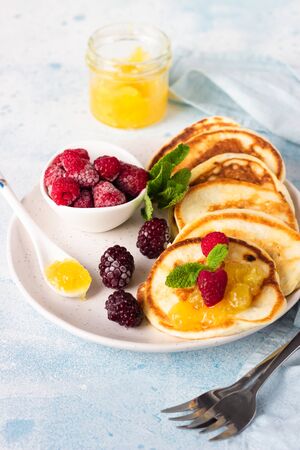 Pancakes with orange jam, frozen berries (raspberries and blackberries) and mint on light blue stone background. Breakfastの写真素材